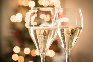 Zwei Gläser Sekt mit festlichen, verschwommenen Lichtern im Hintergrund.