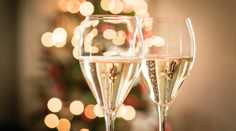 Zwei Gläser Sekt mit festlichen, verschwommenen Lichtern im Hintergrund.